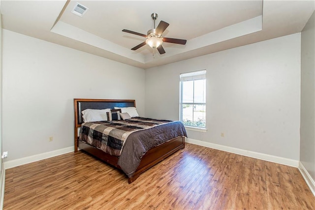 bedroom featuring wood finished floors, a ceiling fan, visible vents, baseboards, and a tray ceiling