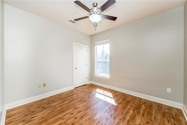 unfurnished room with a ceiling fan, visible vents, baseboards, and wood finished floors