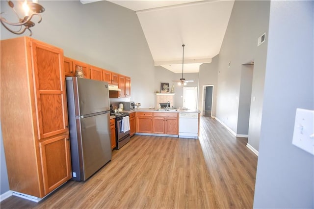 kitchen with high vaulted ceiling, under cabinet range hood, a peninsula, a sink, and appliances with stainless steel finishes