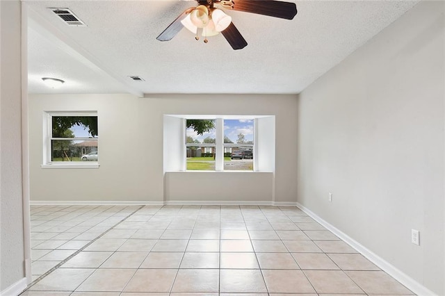 spare room featuring light tile patterned floors, baseboards, visible vents, and a textured ceiling