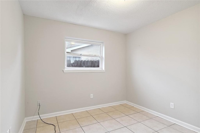 spare room featuring light tile patterned floors, baseboards, and a textured ceiling