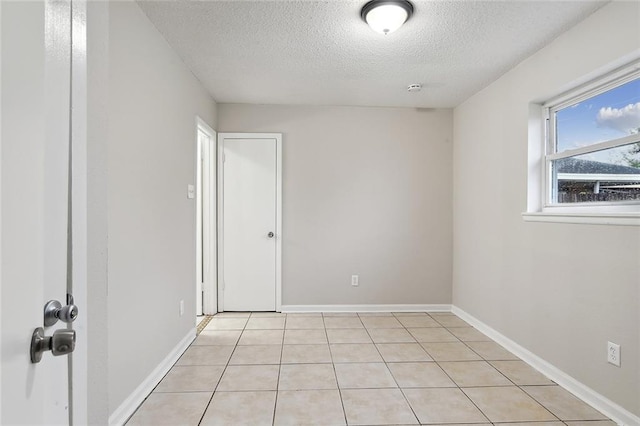 spare room with light tile patterned flooring, a textured ceiling, and baseboards