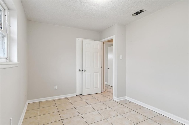 interior space with a textured ceiling, light tile patterned floors, visible vents, and baseboards