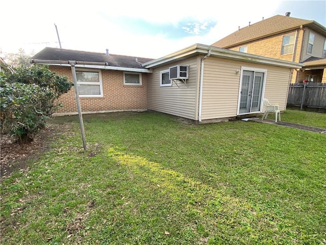 rear view of property featuring a wall unit AC, fence, brick siding, and a lawn