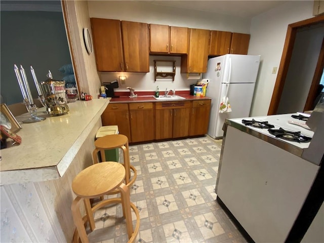 kitchen with light floors, brown cabinetry, freestanding refrigerator, a sink, and range