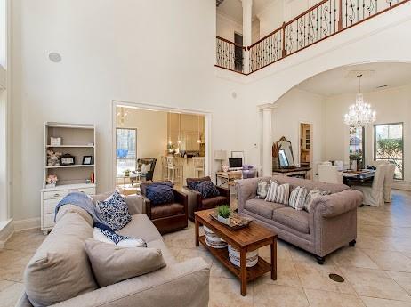 living area featuring a chandelier, arched walkways, decorative columns, and a towering ceiling