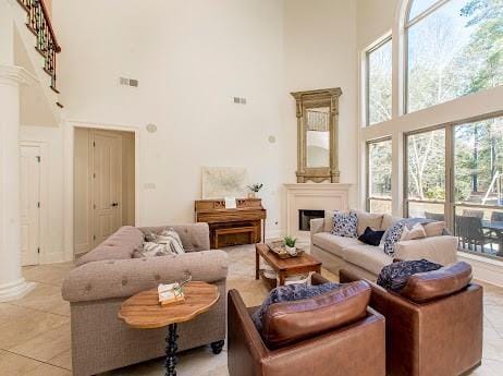 living area featuring visible vents, a fireplace, a towering ceiling, and decorative columns