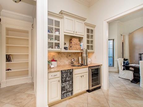 bar featuring light tile patterned floors, beverage cooler, a sink, ornamental molding, and tasteful backsplash