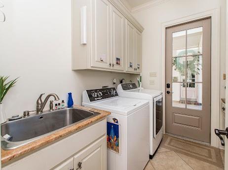 laundry room with cabinet space, ornamental molding, separate washer and dryer, a sink, and light tile patterned flooring