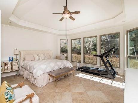 bedroom featuring ornamental molding, a tray ceiling, multiple windows, and light tile patterned floors