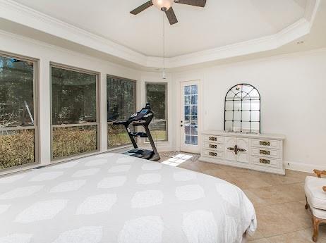 tiled bedroom with ceiling fan, baseboards, access to exterior, ornamental molding, and a tray ceiling