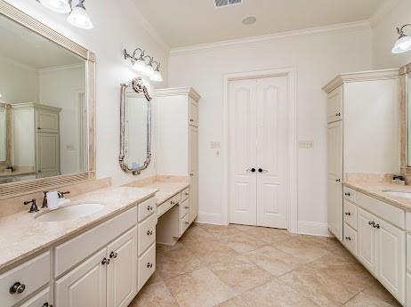 full bathroom featuring baseboards, two vanities, a sink, and crown molding