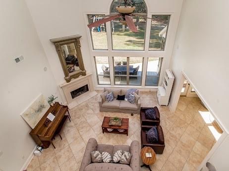 living room with a fireplace, light tile patterned floors, a high ceiling, a ceiling fan, and baseboards