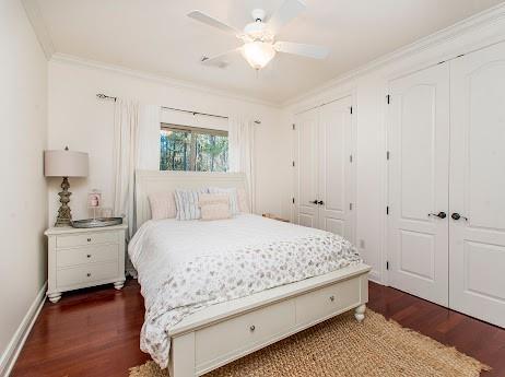 bedroom featuring crown molding, baseboards, dark wood-type flooring, and two closets