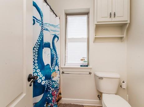 bathroom featuring toilet, curtained shower, and baseboards