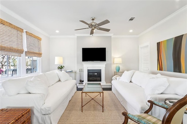 living area featuring ornamental molding, a glass covered fireplace, visible vents, and a ceiling fan