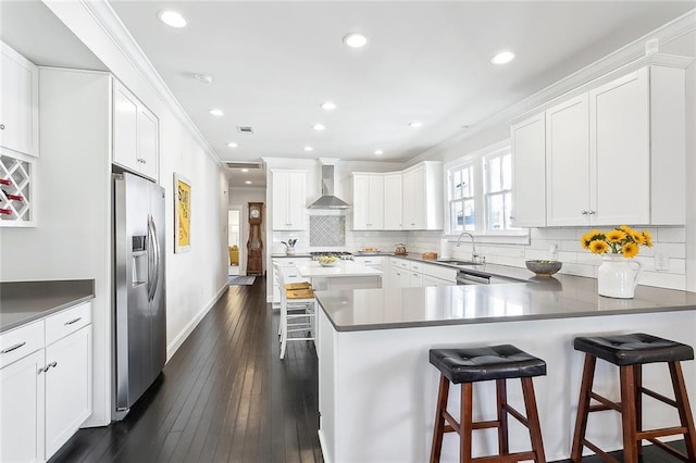 kitchen featuring appliances with stainless steel finishes, ornamental molding, white cabinets, a sink, and wall chimney range hood