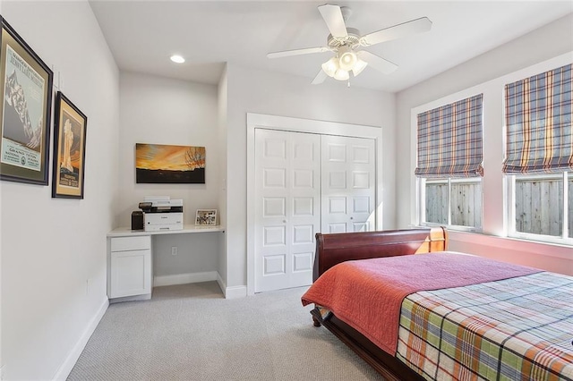 bedroom with a closet, light colored carpet, built in study area, ceiling fan, and baseboards