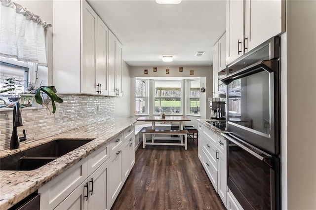 kitchen featuring black appliances, white cabinetry, backsplash, and a sink