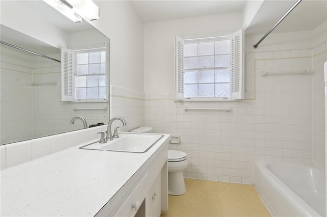 full bath featuring toilet, a wainscoted wall, vanity, tile walls, and  shower combination