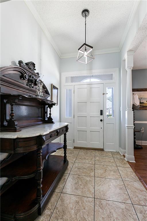 foyer with light tile patterned floors, decorative columns, ornamental molding, and a textured ceiling