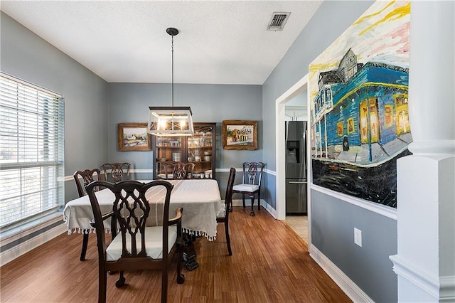 dining space featuring visible vents, a textured ceiling, baseboards, and wood finished floors