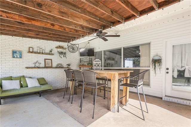 exterior space featuring a ceiling fan, wooden ceiling, brick wall, concrete floors, and beam ceiling