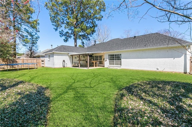 rear view of house with a trampoline, brick siding, a patio, a lawn, and fence