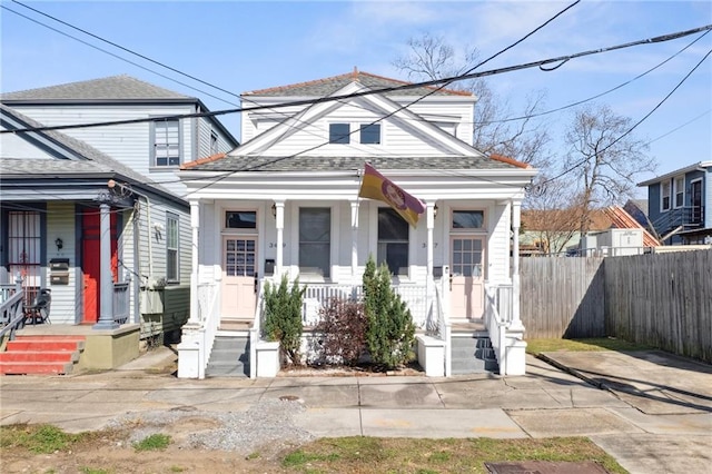 view of front facade featuring a porch, roof with shingles, and fence