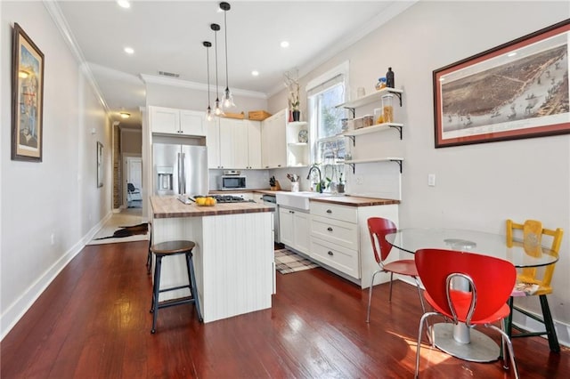 kitchen featuring visible vents, appliances with stainless steel finishes, a breakfast bar area, a center island, and wooden counters