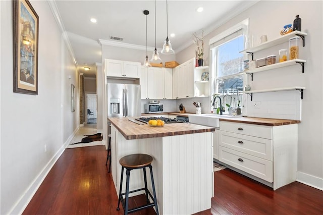 kitchen featuring stainless steel appliances, butcher block counters, a sink, and open shelves