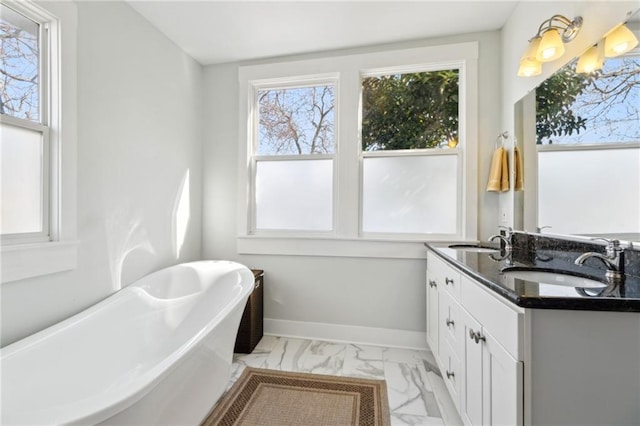 bathroom with marble finish floor, a freestanding tub, a sink, and baseboards