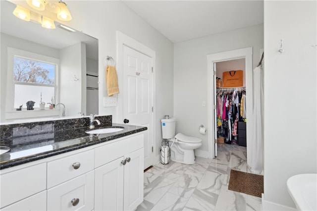 full bath featuring toilet, vanity, baseboards, marble finish floor, and a spacious closet