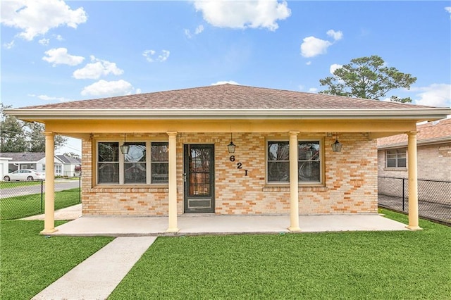 back of house with roof with shingles, fence, a lawn, and brick siding