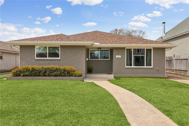 single story home featuring roof with shingles, fence, a front lawn, and brick siding