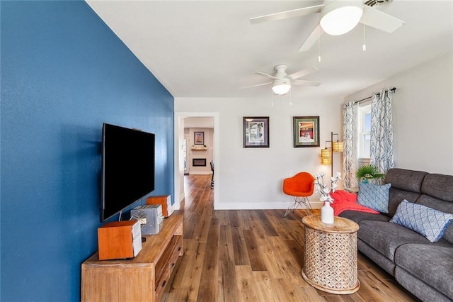 living room featuring a ceiling fan, baseboards, and wood finished floors