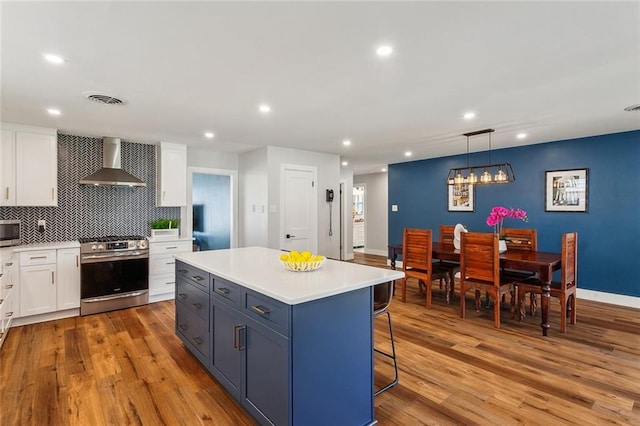 kitchen featuring visible vents, white cabinetry, appliances with stainless steel finishes, light wood-type flooring, and wall chimney exhaust hood