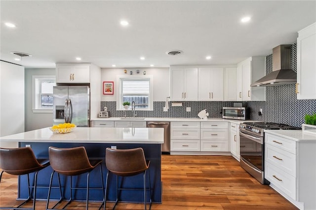 kitchen with wall chimney exhaust hood, appliances with stainless steel finishes, light wood-style flooring, and a breakfast bar