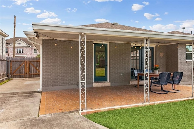 rear view of property with brick siding, fence, roof with shingles, a gate, and a patio area