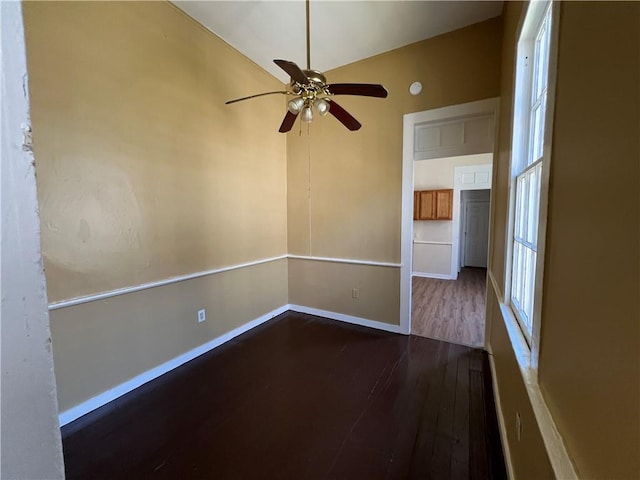 empty room with dark wood finished floors, a ceiling fan, and baseboards