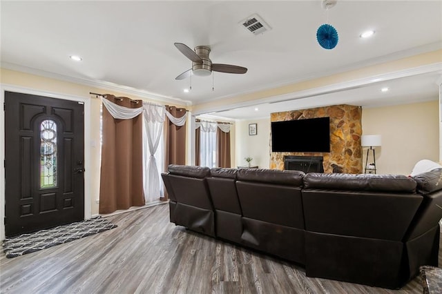 living area featuring a fireplace, wood finished floors, a ceiling fan, visible vents, and crown molding