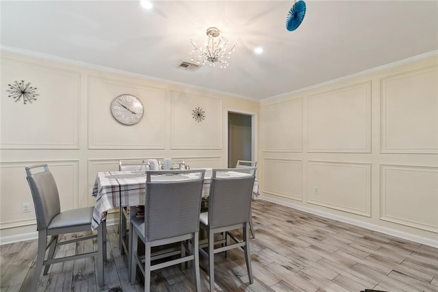 dining area with a notable chandelier, light wood finished floors, visible vents, a decorative wall, and ornamental molding