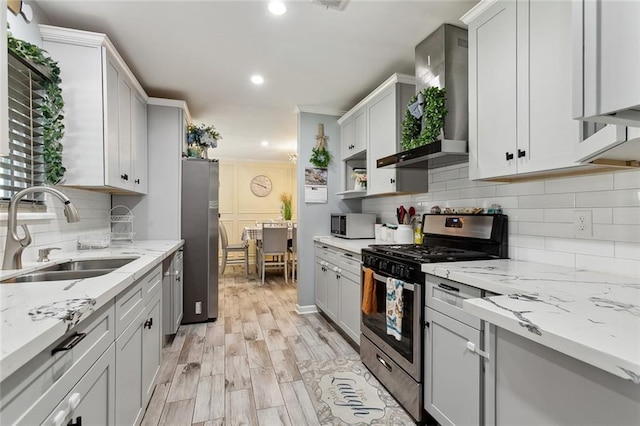 kitchen featuring light stone counters, a sink, appliances with stainless steel finishes, decorative backsplash, and light wood finished floors