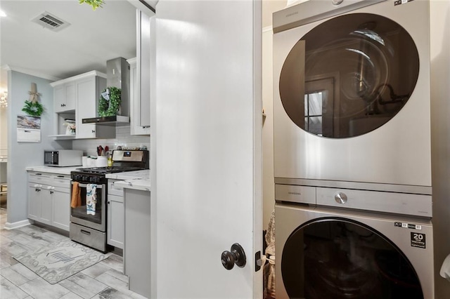 laundry room featuring ornamental molding, laundry area, visible vents, and stacked washing maching and dryer