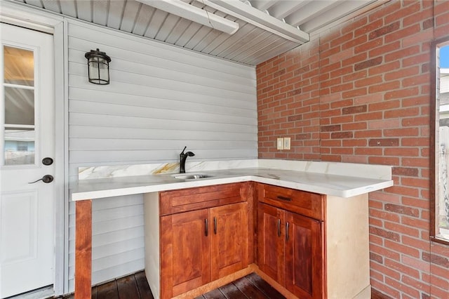 kitchen featuring dark wood-type flooring, brick wall, brown cabinets, and a sink