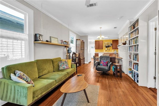 living room with an inviting chandelier, wood-type flooring, visible vents, and crown molding