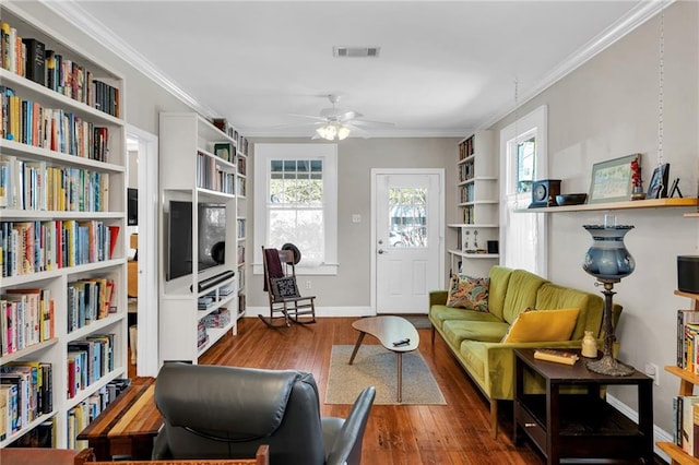 living area with crown molding, wood-type flooring, visible vents, a ceiling fan, and baseboards