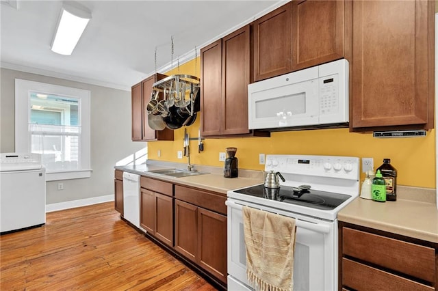 kitchen with light countertops, light wood-style flooring, a sink, washer / dryer, and white appliances