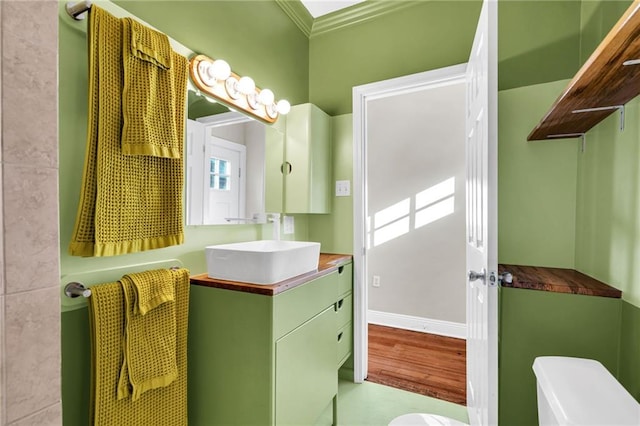 bathroom featuring toilet, wood finished floors, vanity, baseboards, and crown molding