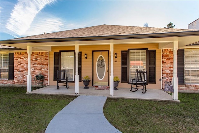 entrance to property with a porch, brick siding, and a yard